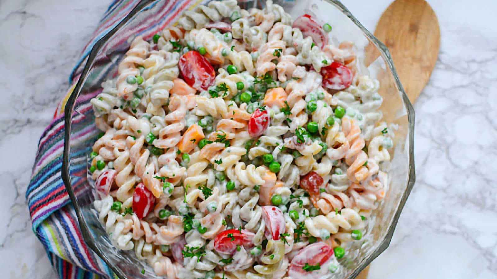 Bacon ranch pasta salad in a clear bowl with a striped towel.