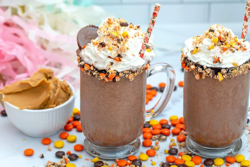 Glasses with peanut butter hot chocolate topped with whipped cream and sprinkles.