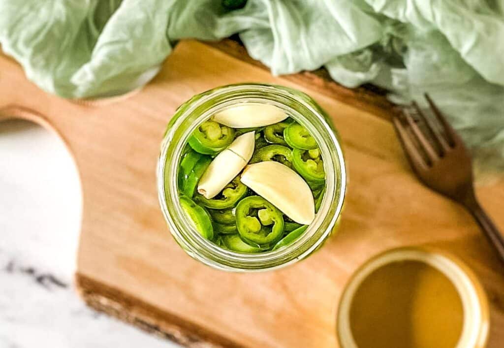 Pickled serrano peppers and garlic cloves in a glass jar.