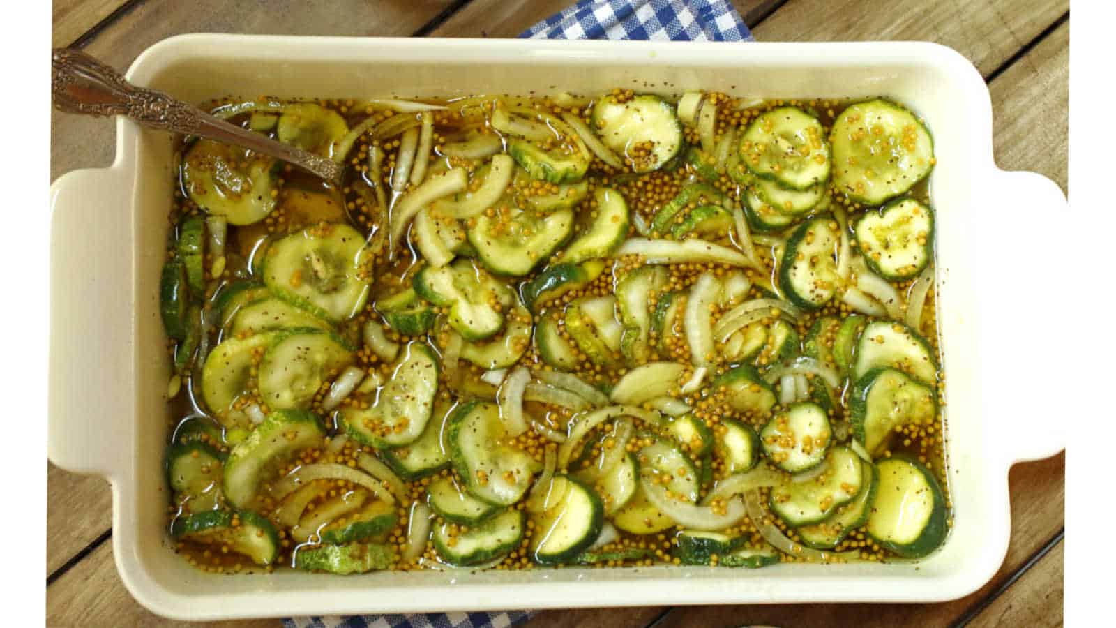 Bread and butter pickles in brine in a white dish.