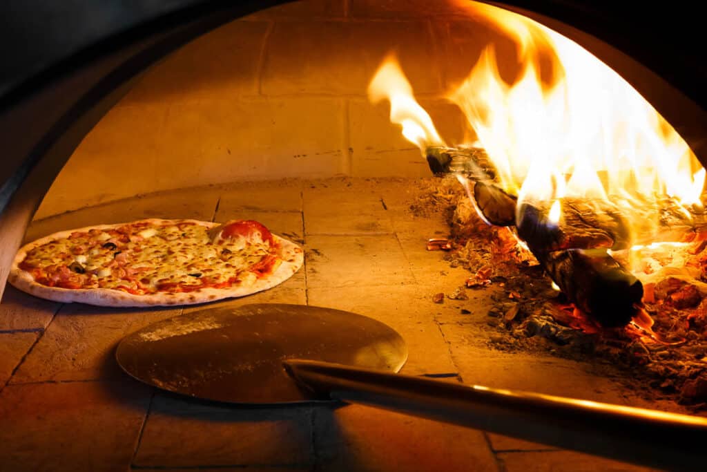 Close up pizza in firewood oven with flame behind