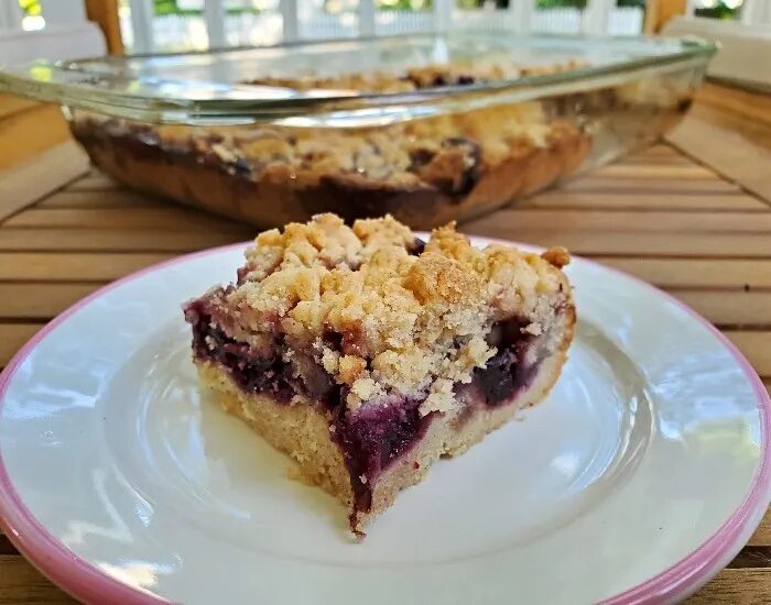 Image shows a small place with a cherry crumb bar on it and hte full pan behind it.