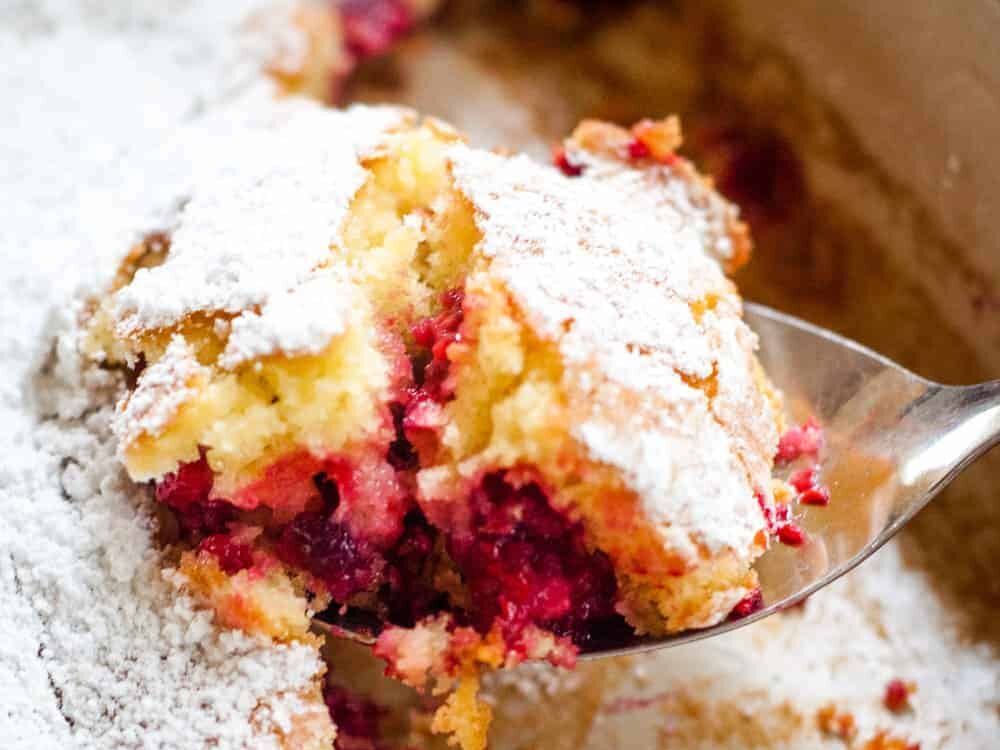 Raspberry buckle in a pan with a spoon scooping some out of the pan.