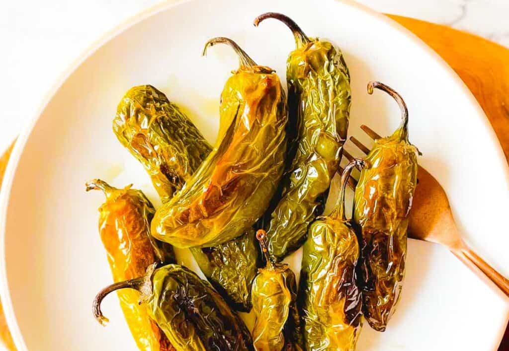 Roasted jalapenos on a white plate with a fork.