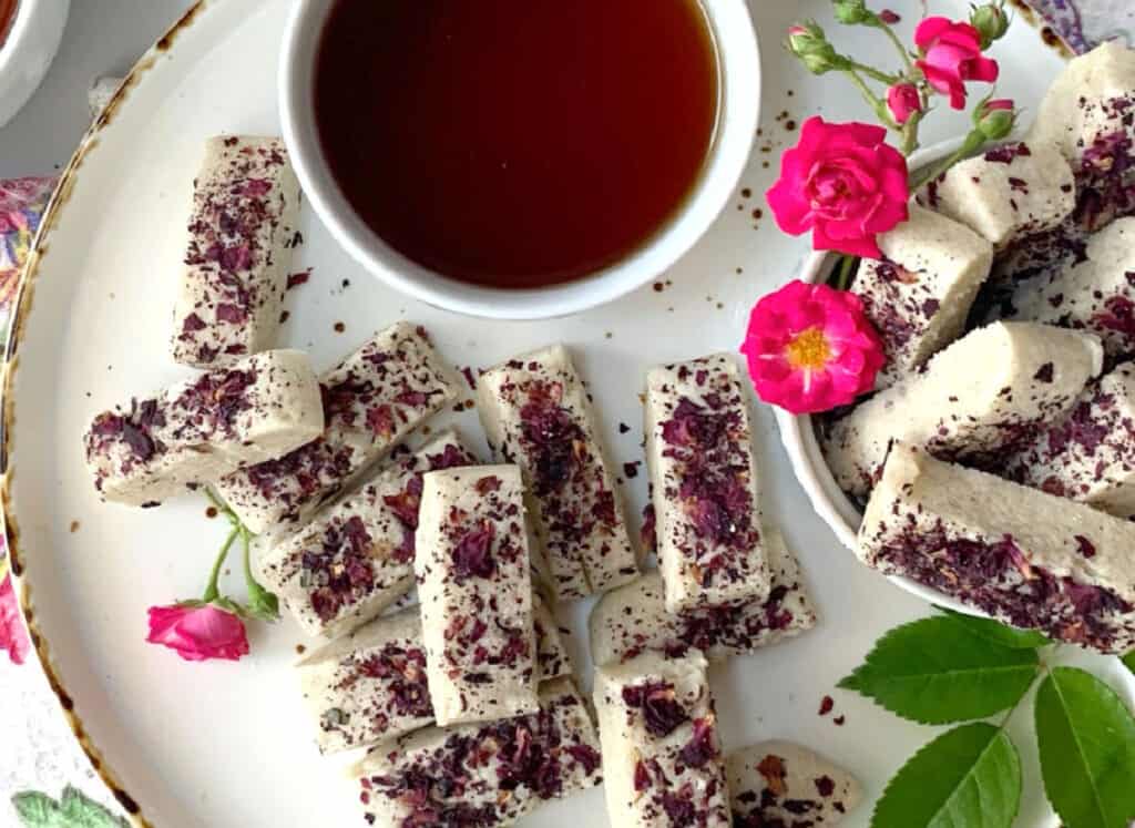 Rose shortbreads on a white plate with a cup of tea.