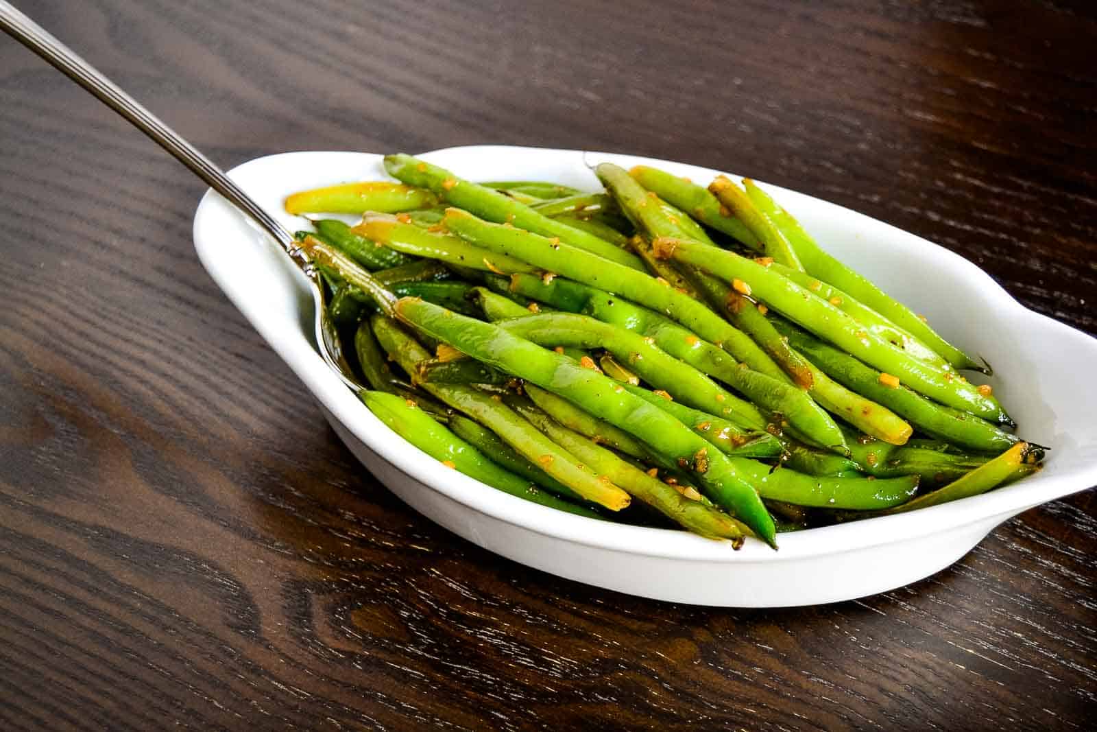 Screaming skillet green beans in a white bowl on a wooden table.