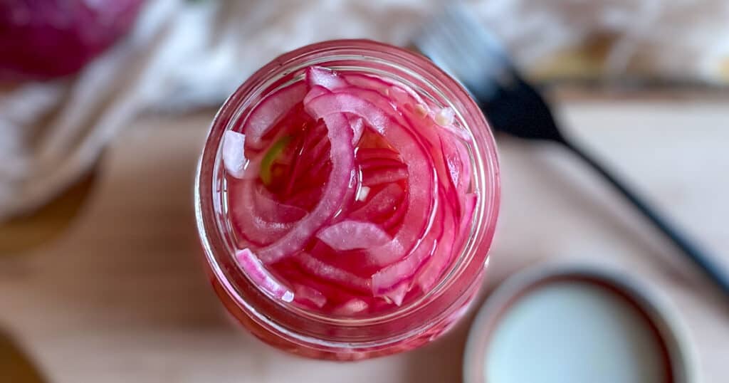 Closeup of spicy pickled onions in a glass jar.