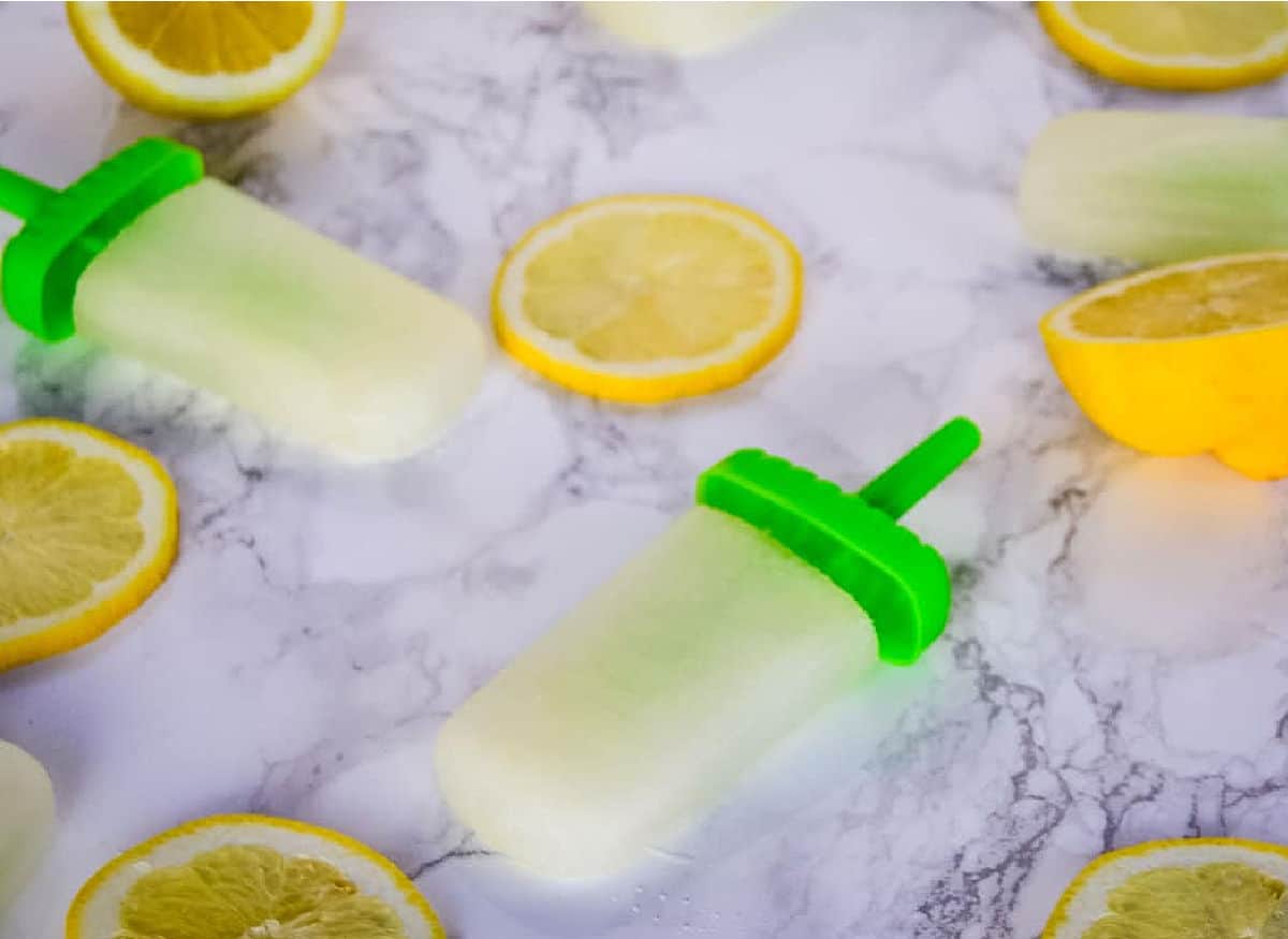 Spiked lemonade popsicles on a marble background next to lemons.
