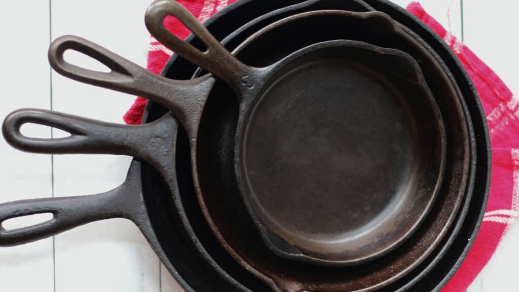 Four sizes of cast iron skillets on a red towel.
