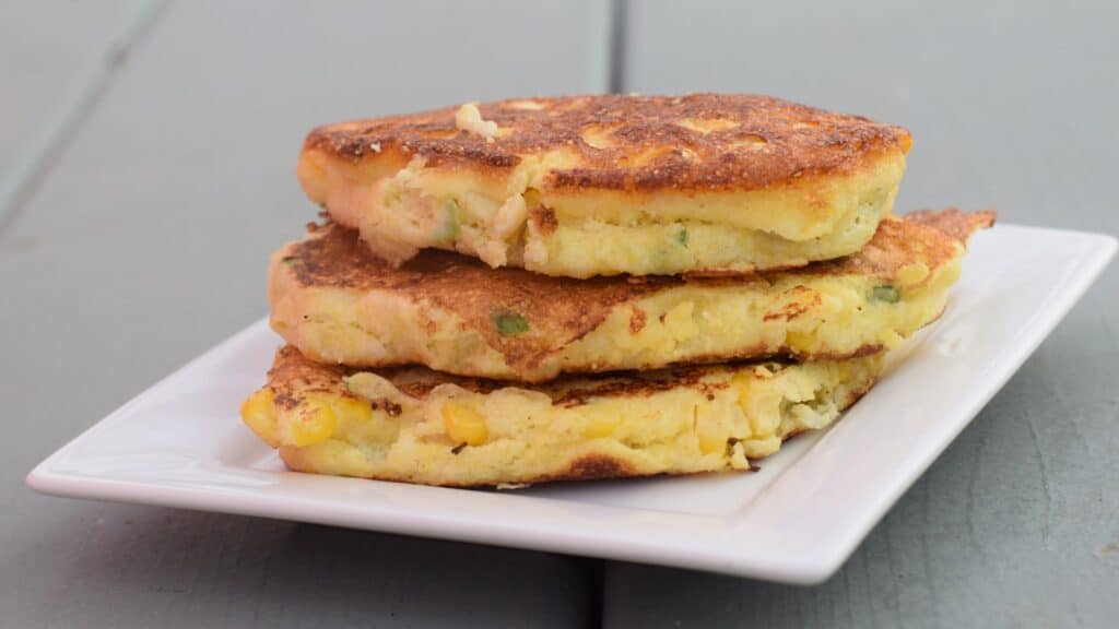 Stack of three corn fritters on a small white plate.