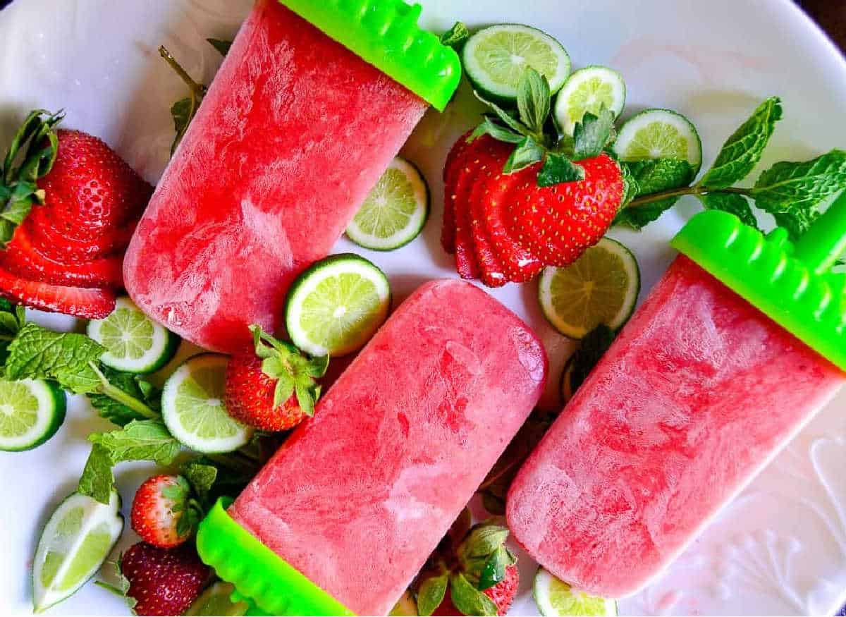 Strawberry mojito wine popsicles on a white plate with strawberries lime and mint leaves.