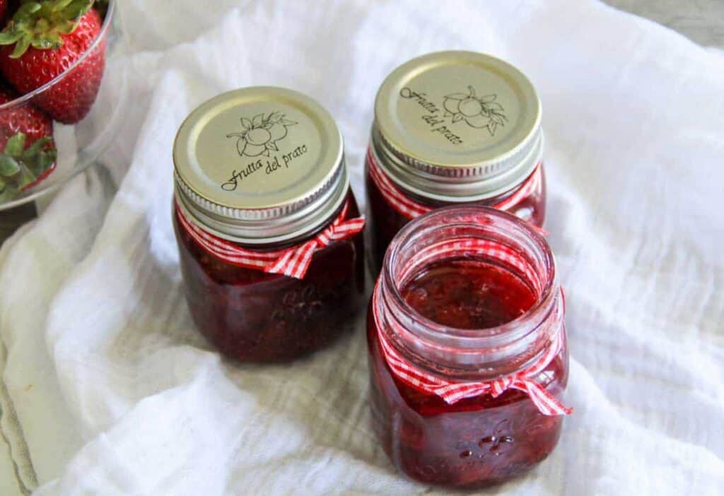Three jars of strawberry syrup on a white cloth.