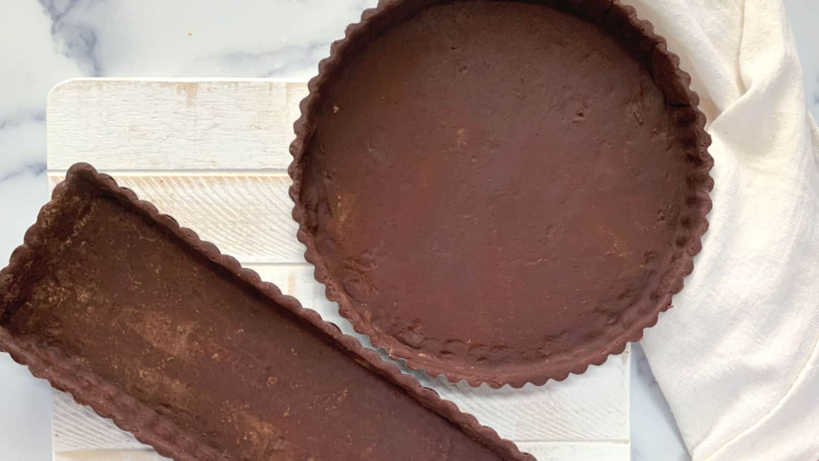 Two chocolate tart crusts on a white board.