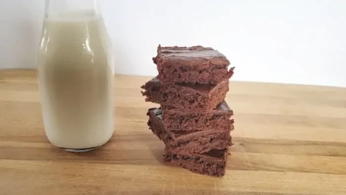 Texas sheetcake brownies stacked on a wooden board sitting next to a small jug of milk.
