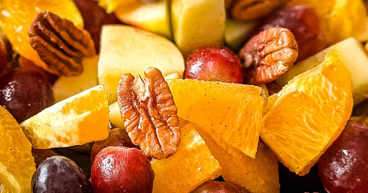 Closeup shot of a fruit salad with oranges, grapes, apple, and walnuts.