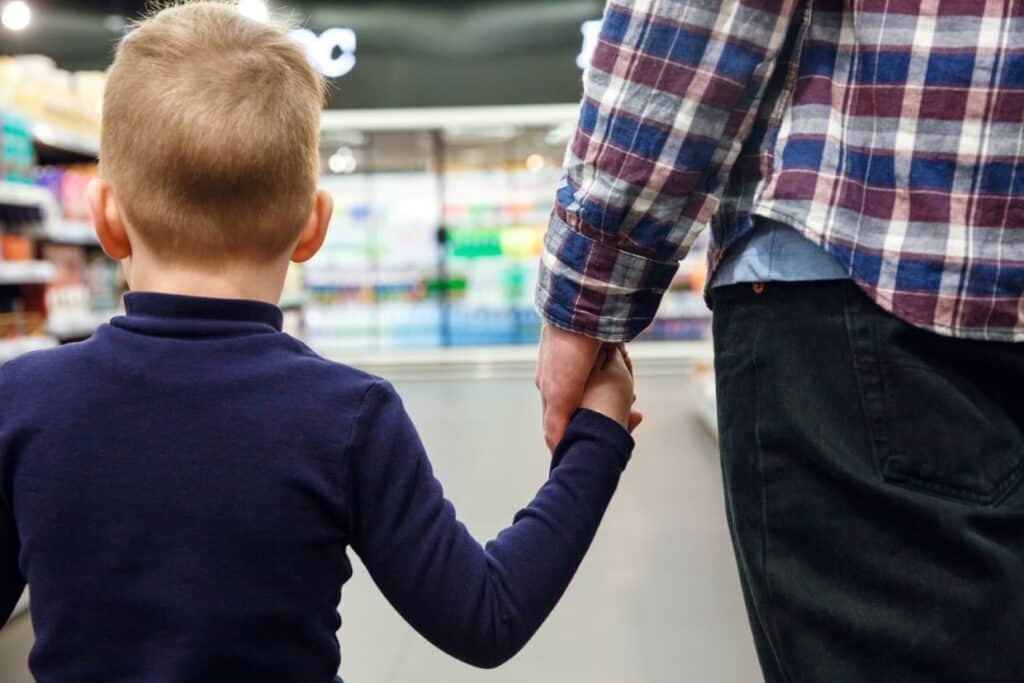 Toddler holding hand with parent walking in store.