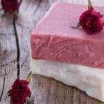 valentine's day rose soap two bars close up view one white and one pink stacked with rose buds and wooden background