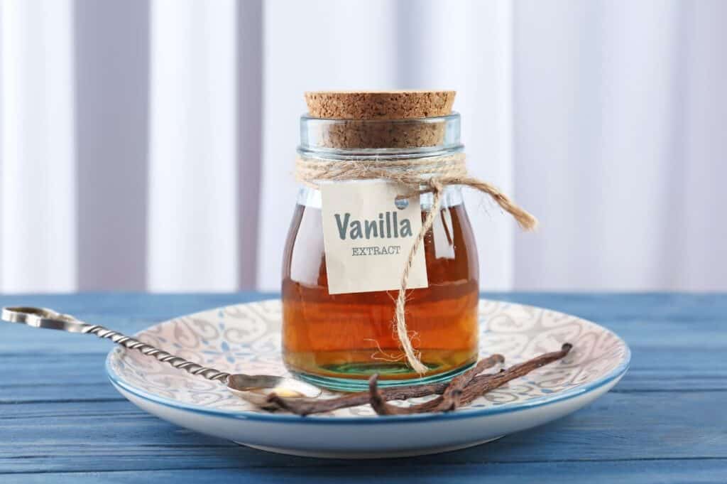 A bottle of vanilla extract on a saucer with vanilla beans.