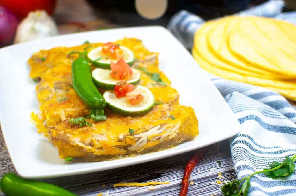 Enchiladas on a plate garnished with lime slices and chile peppers.