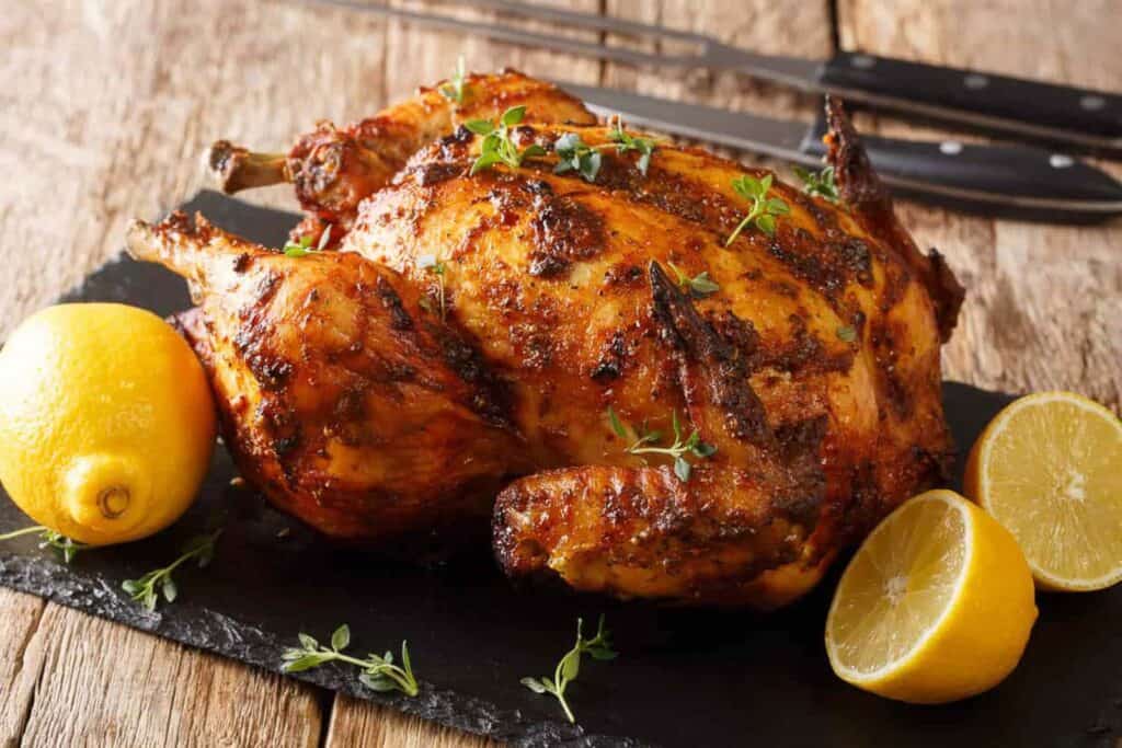 Whole roasted chicken on a piece of slate with lemons.