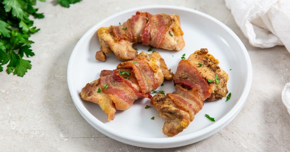 Easy Air Fryer Bacon Wrapped Chicken Thighs on a plate with parsley and a fork.