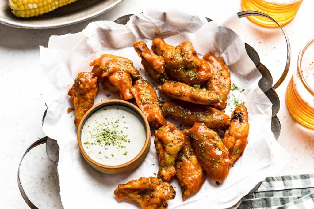 a basket of glazed chicken wings with a glass bowl of ranch sauce.
