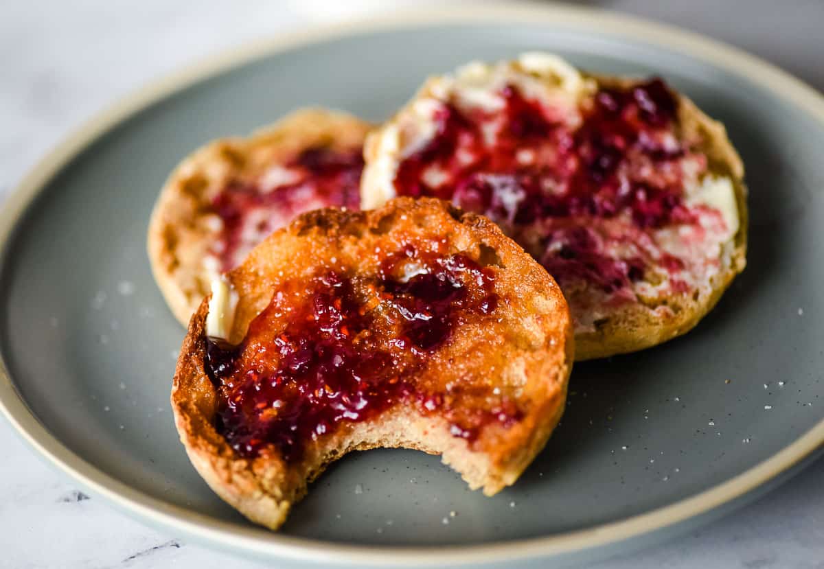 Three English muffins with butter and jam sit on a blue plate.