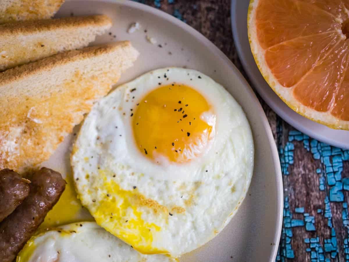 Fried egg on a plate with toast, sausage links and grapefruit.