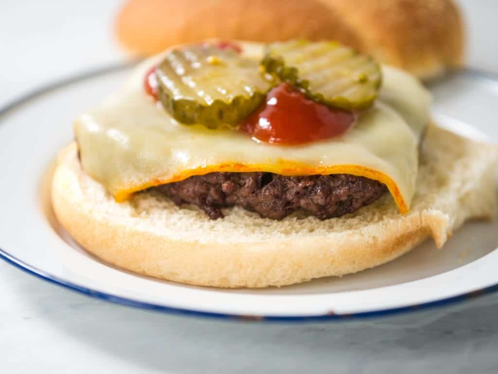 A burger topped with melted cheese, ketchup and pickles.