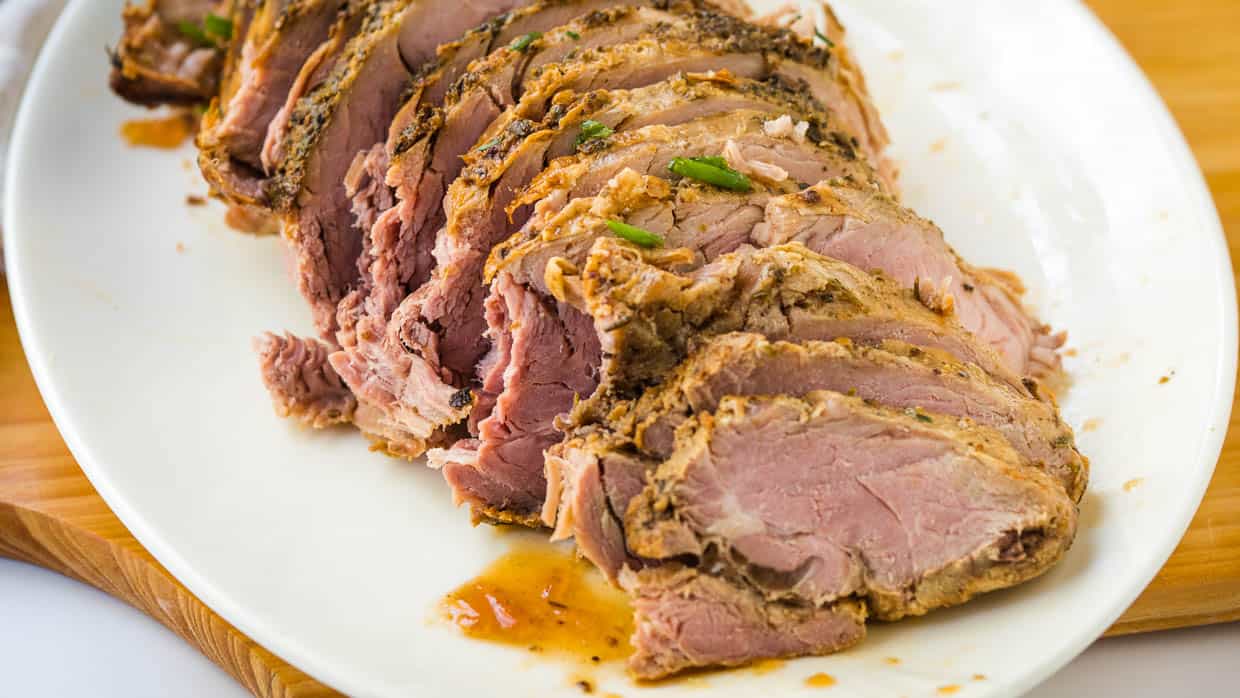 Sliced pork loin on white plate with herbs.
