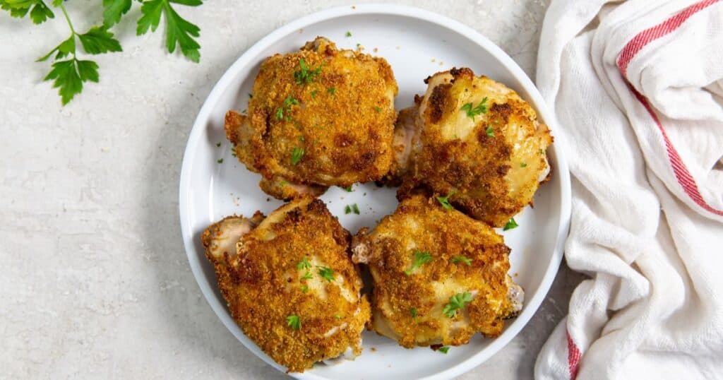 air fryer shake and bake chicken thighs on a white plate with a napkin and parsley.