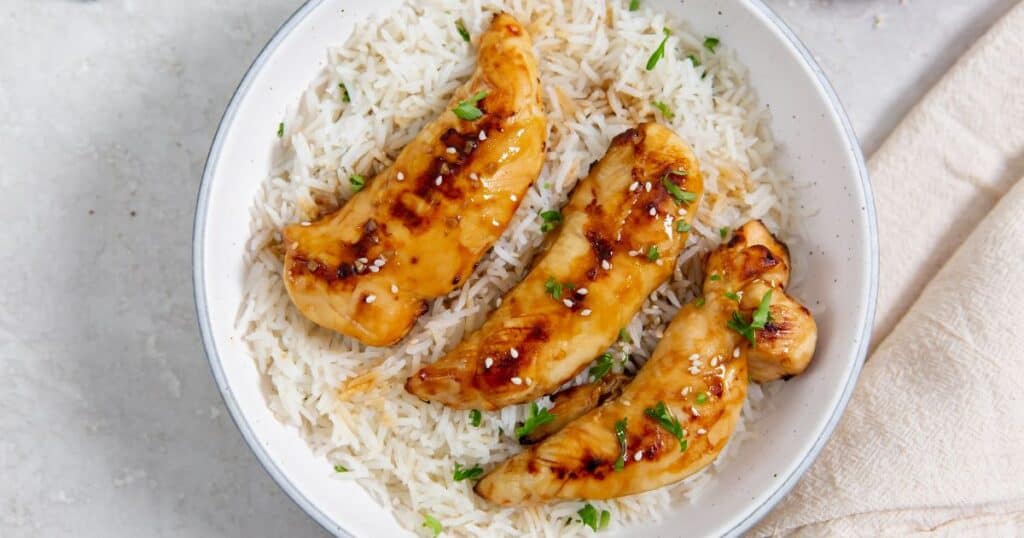 teriyaki chicken tenders in a white bowl with rice.