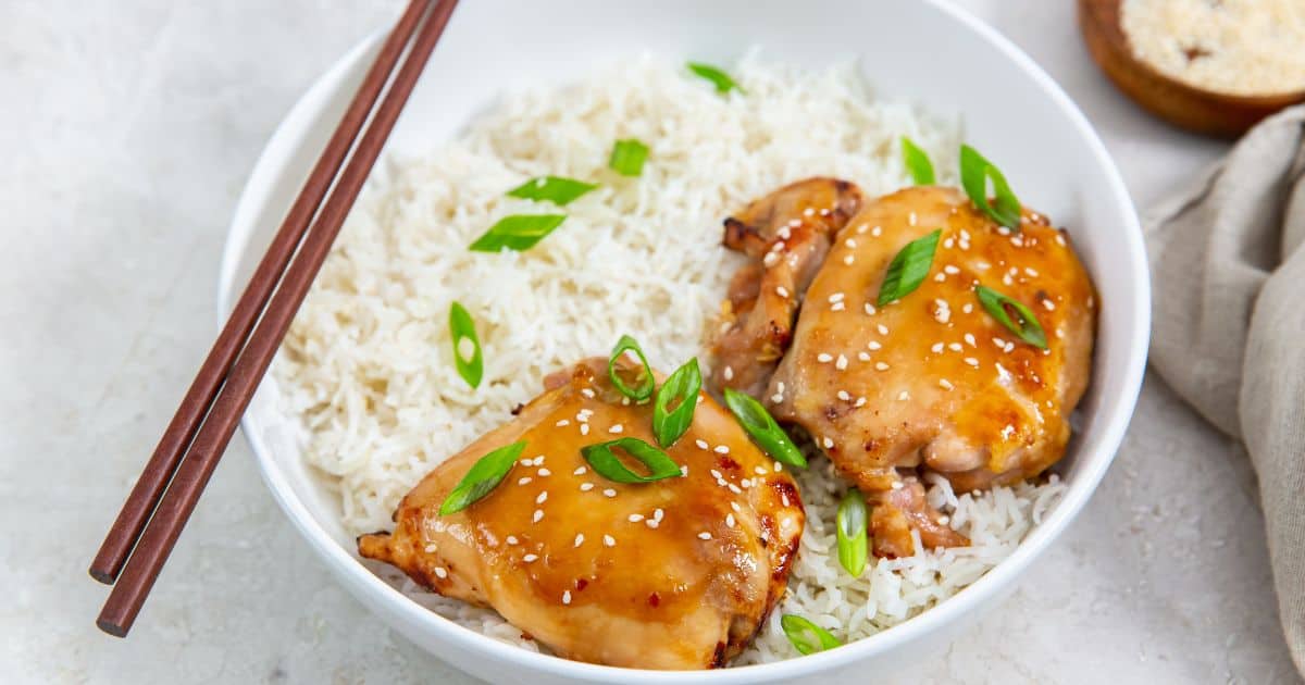 Easy Air Fryer Teriyaki Chicken Thighs in a white bowl with white rice, green onions, and sesame seeds.