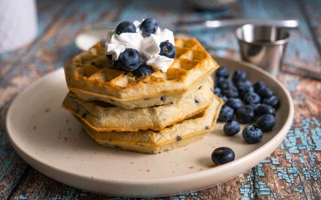 Air fryer frozen waffles topped with whipped cream on a plate with blueberries.