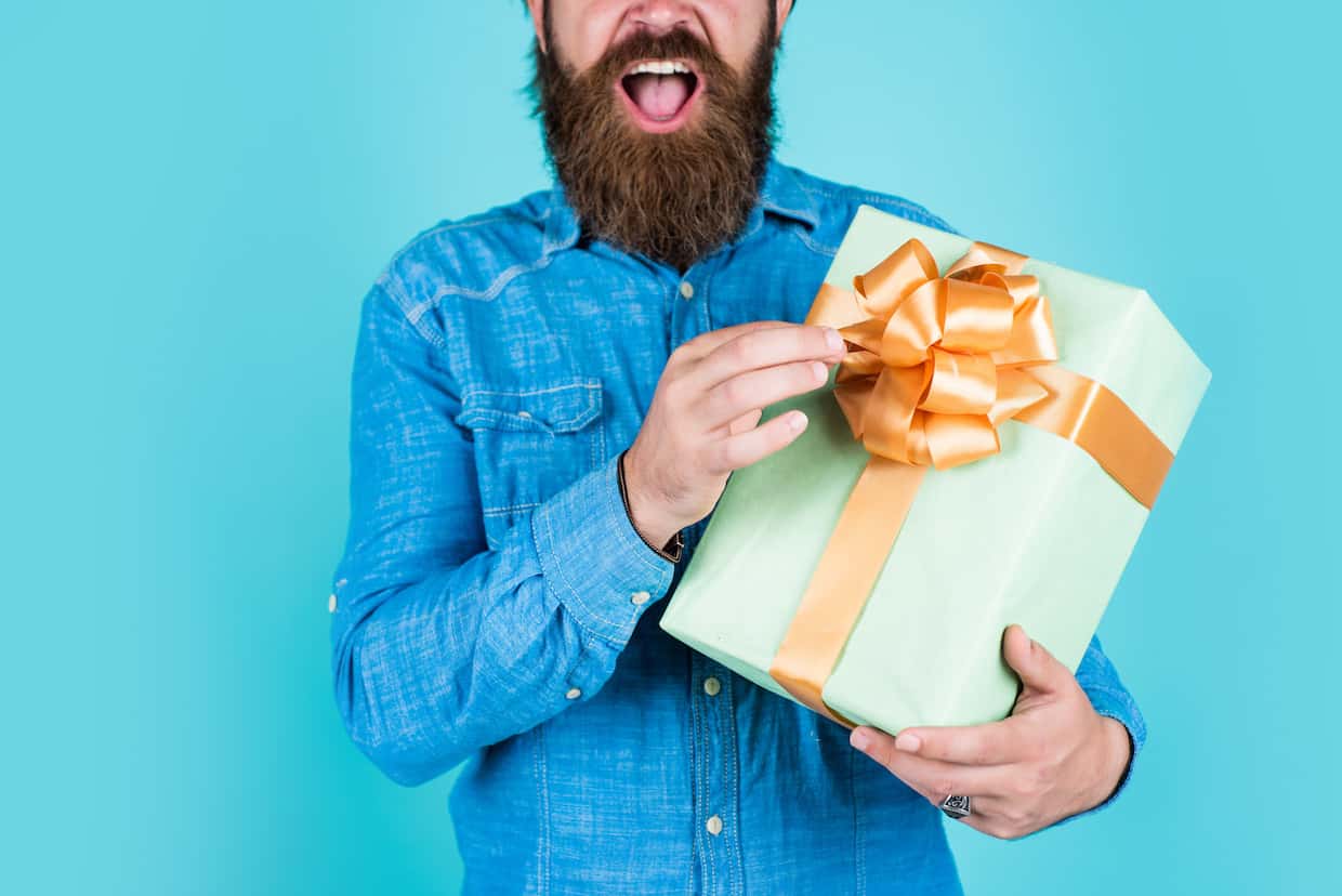 Hipster dude with beard in denim shirt holding a wrapped present with a bow.
