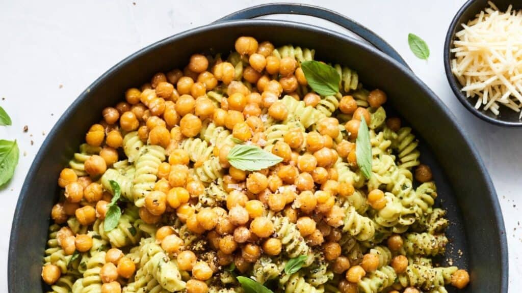 A black cast iron skilled filled with green pasta and chickpeas.