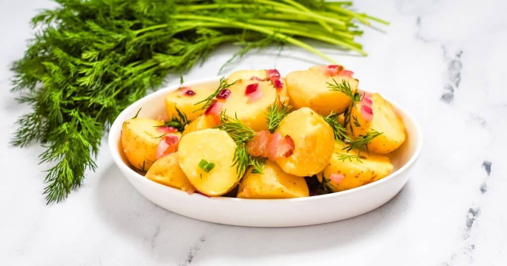 Bavarian potato salad in a white dish surrounded by fresh dill.