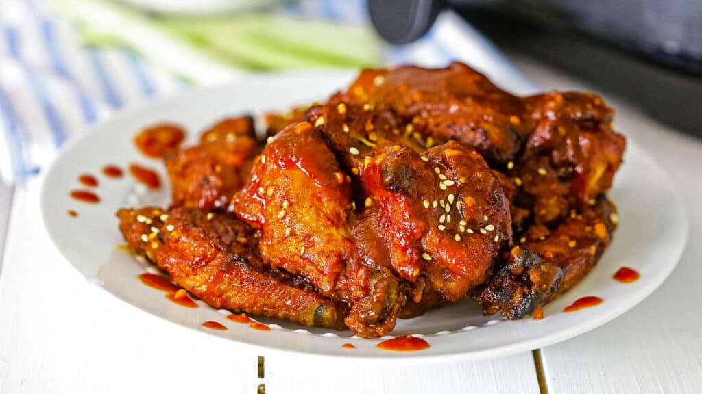 Plate of BBQ chicken wings in front of an air fryer.