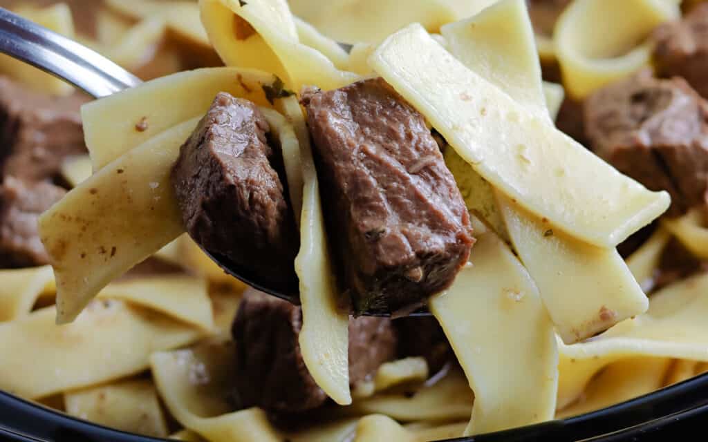 Closeup of a beef on a fork with egg noodles.