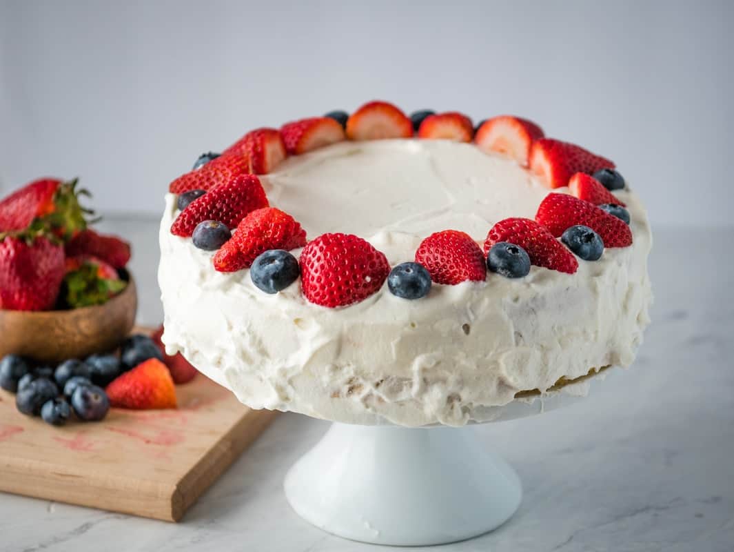Norwegian cream cake on a cake stand decorated with strawberries and blueberries.