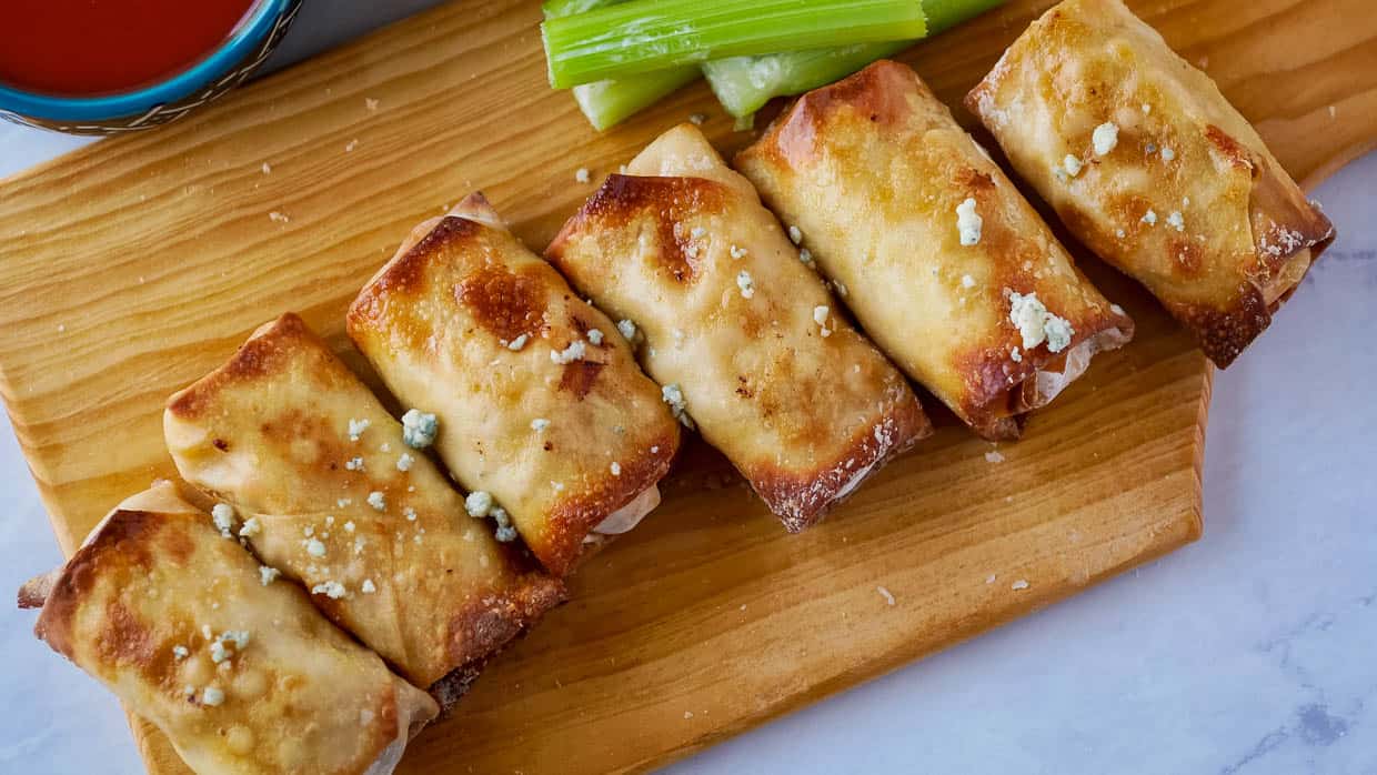 Buffalo chicken egg rolls on a wooden cutting board with celery and sprinkled with blue cheese.