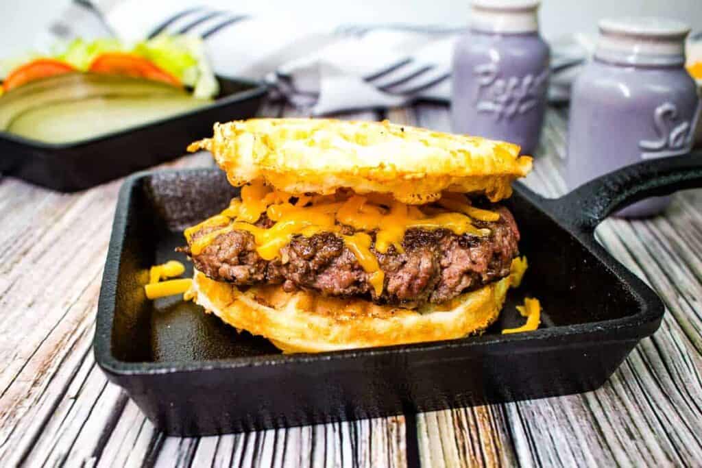 A butter Burger on a chaffle in a black dish with vegetables in the background.