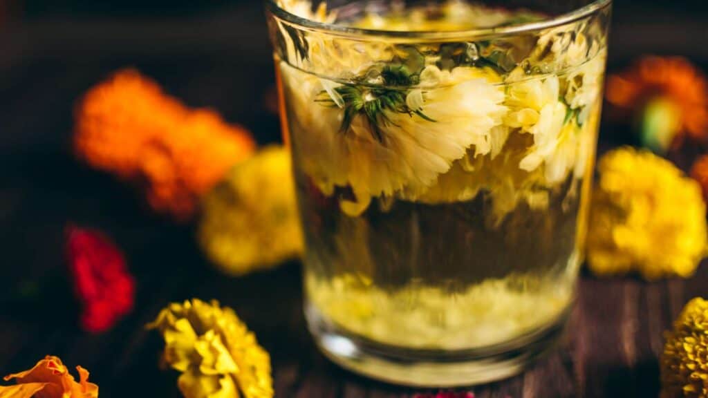A clear glass filled with a clear liquid and fresh yellow flowers.