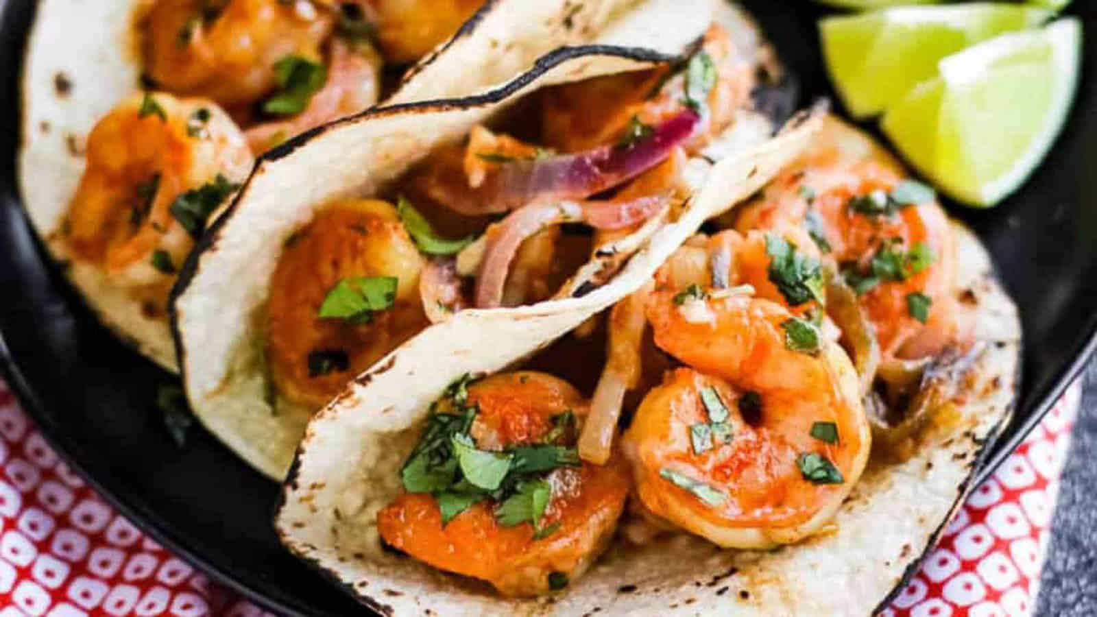 Shrimp stuffed into soft corn tortillas with lime wedges on the side.