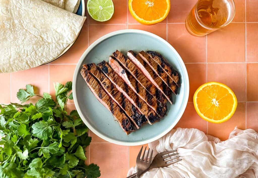 Carne asada on a blue plate surrounded by oranges, limes, and cilantro.