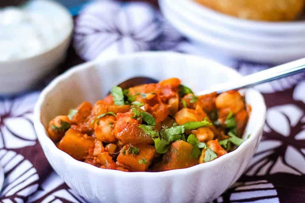 Chana Aloo Masala in a white bowl with a spoon.