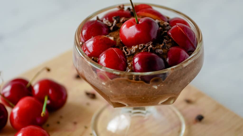 Chocolate chia pudding in a dessert cup with cherries on top.