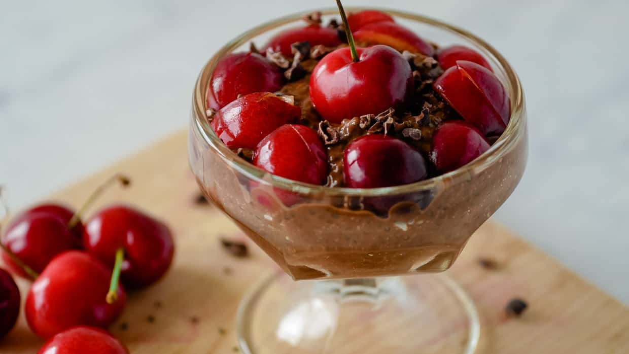 Chocolate chia pudding in a dessert cup with cherries on top.