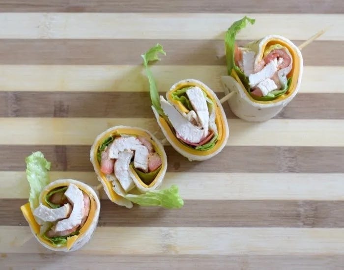 Image shows an overhead shot of chicken taco wraps cut into pinwheels and on a wooden skewer.