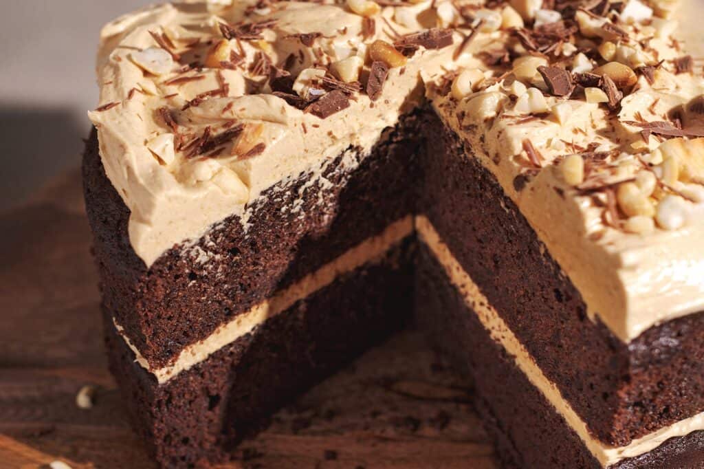 Chocolate layer cake with peanut butter frosting topped with peanuts and shaved chocolate.